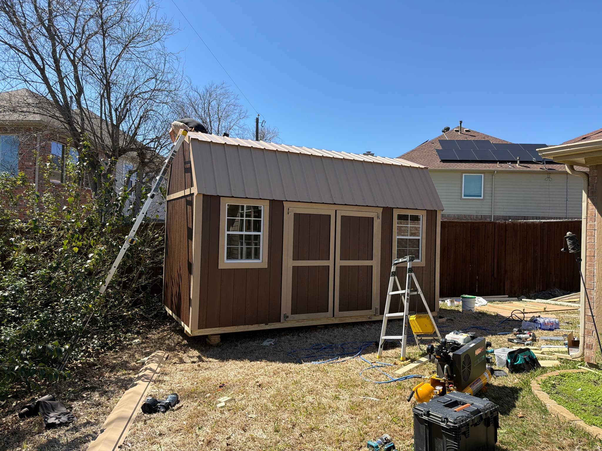 Finished brown 8x16 side lofted barn with metal roof in a Denton backyard at day's end.