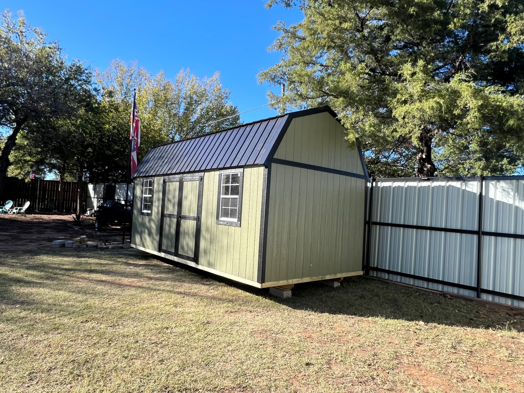 Finished sage green 10 by 20 side lofted barn with dark metal roof in a Henrietta backyard.