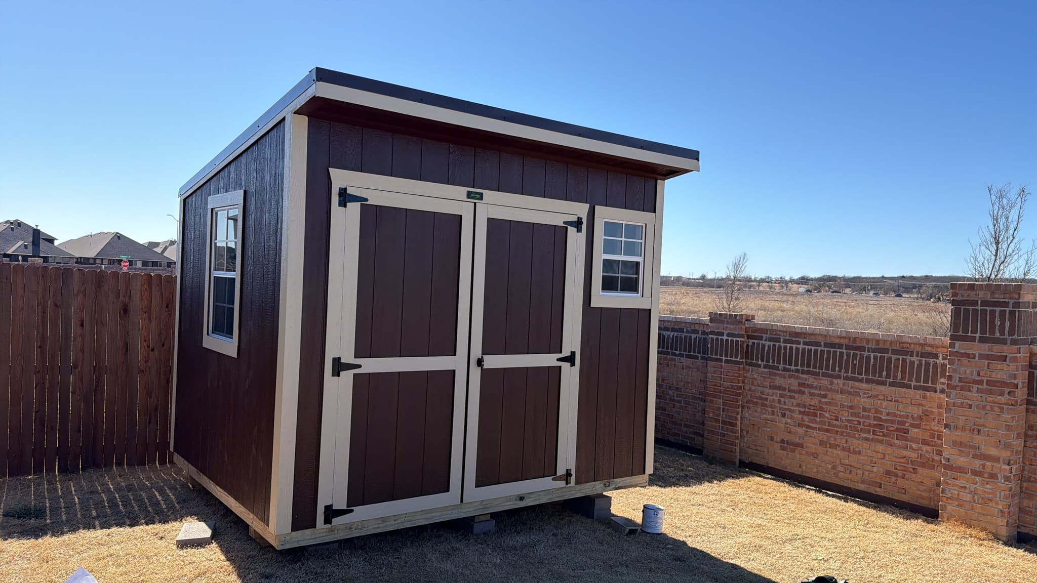 Finished brown 8x12 cottage shed with cream trim, window, and double doors in a Joshua backyard.