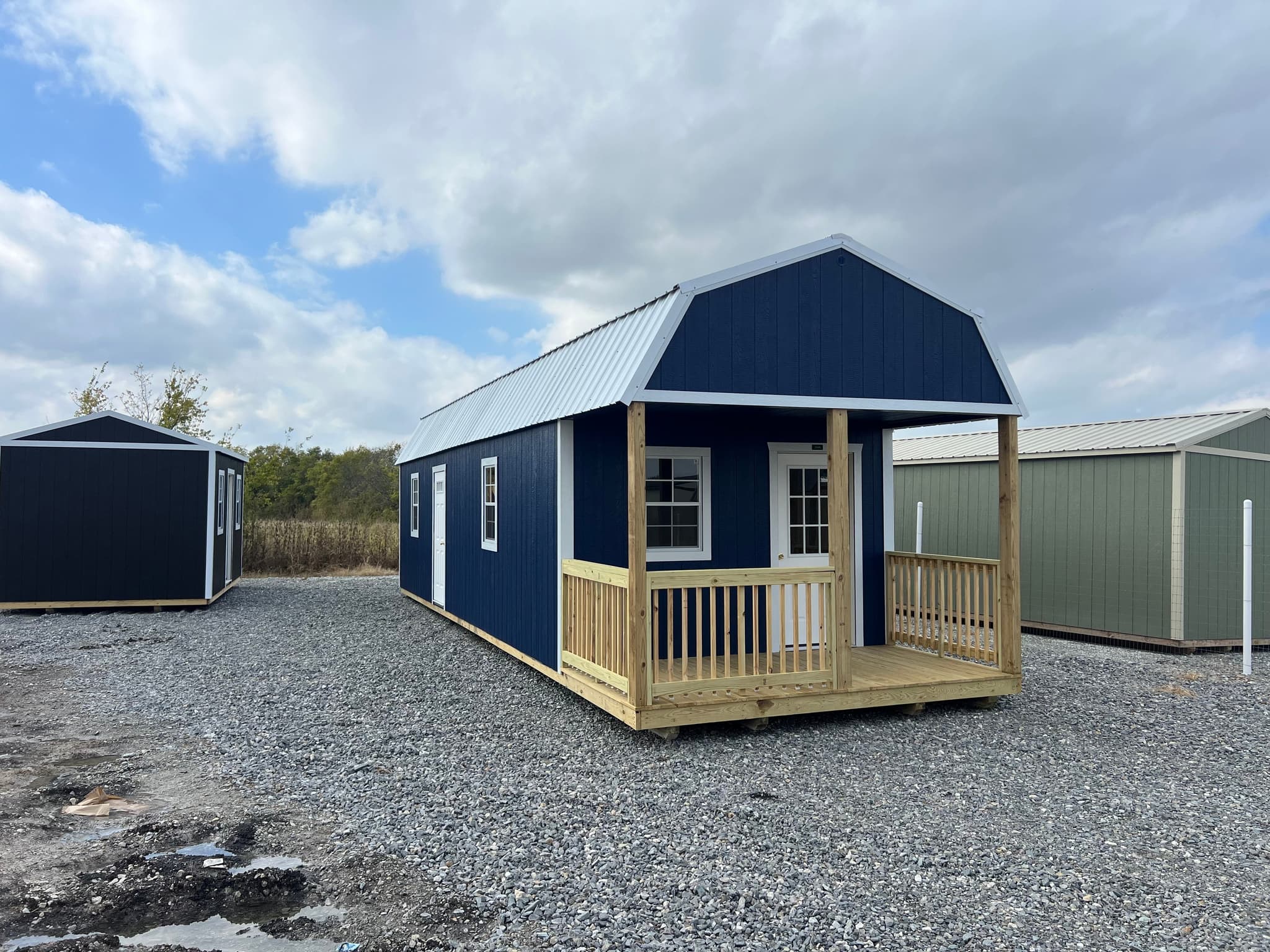 Finished navy 12 by 40 tall wall lofted cabin with covered porch on a gravel dealer lot.